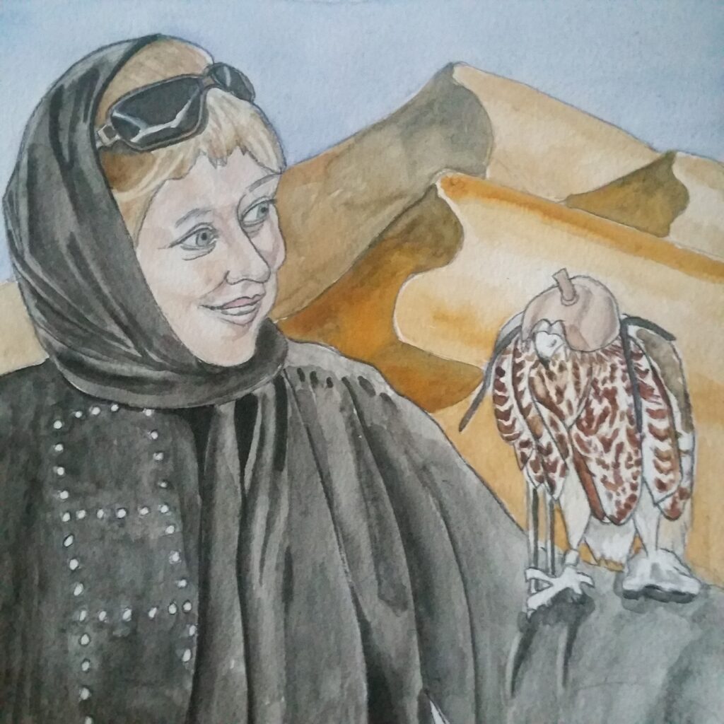 ID Smiling woman with dark blonde hair with fringe. She is wearing a black hijab and abaya. She is turned away from us just slightly more than a 3/4 profile, as she is looking at a hooded falcon perched on her uplifted arm. The falcon is a cultural symbol of the United Arab Emirates