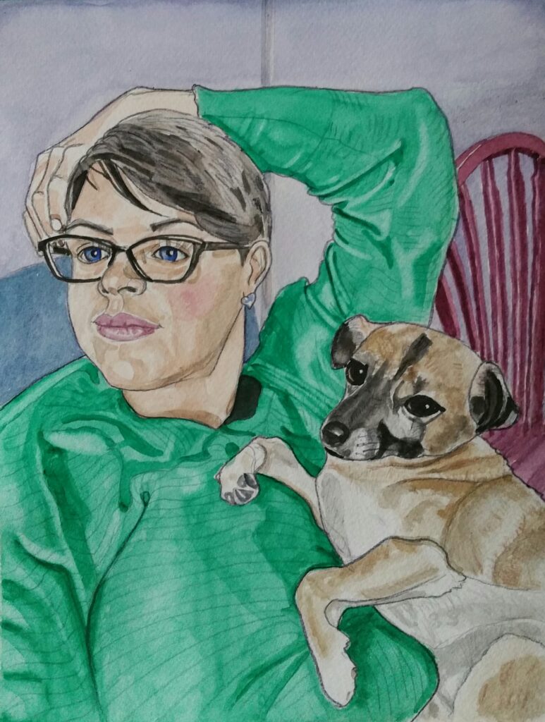 ID Woman sat with her arm resting across the top of her head and her hand dangling by the side of her face, she has her pet dog lying on her chest. She is wearing glasses and has short greying hair layered and swept over to one side. Her long sleeved top is green. Her dog is tan, grey and black and is small with lovely large eyes. In the background can be seen a red/purple spindled chair.