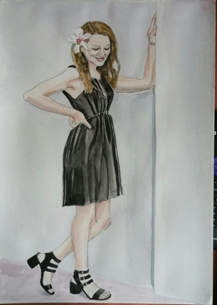 ID Beautiful woman with wavy light brown hair, she is standing with one arm bent and resting on the wall from the elbow. she is looking downwards and smiling and has a lily in her hair and wearing a black dress and black strappy sandals. The dress is above teh knee.
