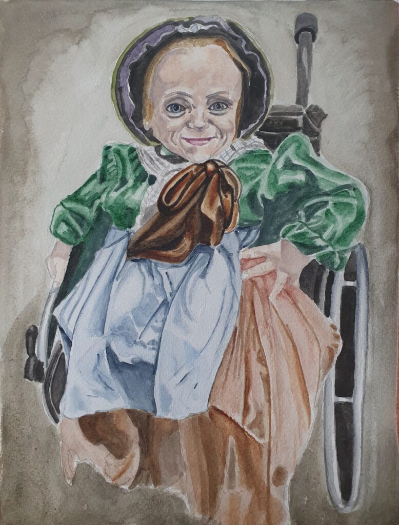 ID Smiling woman sat in wheelchair she is wearing period costume for her role, that comprises bonnet, brown ornately arranged bow, floppy ribbon round neck, a green blousen long sleeved top aa brown skirt and blue apron.