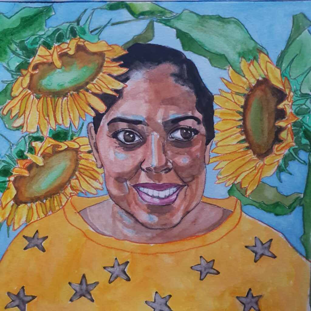 ID Dark haired woman with hair tied back, she has large brown eyes and is smiling - she is wearing a yellow jumper with stars on it and is surrounded by 3 large sunflowers and their leaves. The background in pale blue