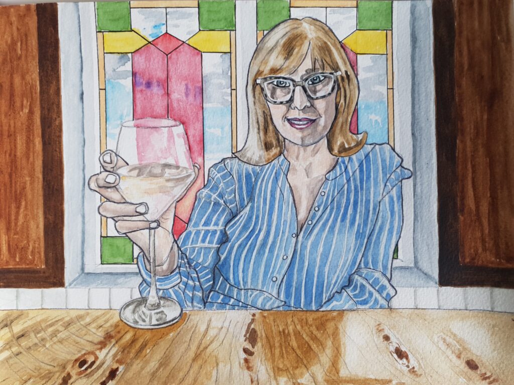 ID Middle aged woman with dark blonde hair, she is wearing glasses and a striped blue and white shirt. she is holding a wine glass forward in a gesture which says "cheers" She is smiling. Behind her are stained glass windows and dark wood panel walls. She is sat behind a wooden table
