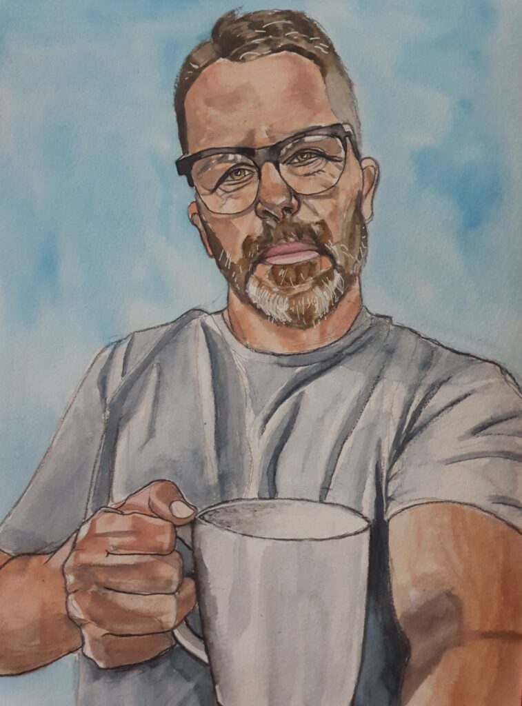 ID Middle aged man with short brown hair with side parting, he has a beard and moustache that is black, brown and grey and is neatly trimmed. He is wearing black framed glasses and a grey T-shirt. He is holding a large white mug in front of himself.