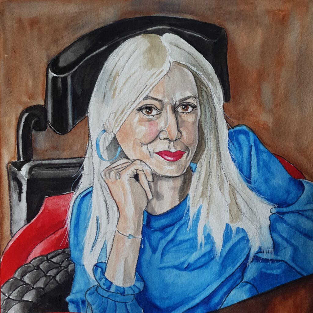 ID Watercolour painting of woman with long blonde hair who has a twinkle in her eye, she is wearing a blue top and is seated in her wheelchair with a table in front of her, between her and the wheelchair you can see a bit of her red coat which is lined with black quilting.