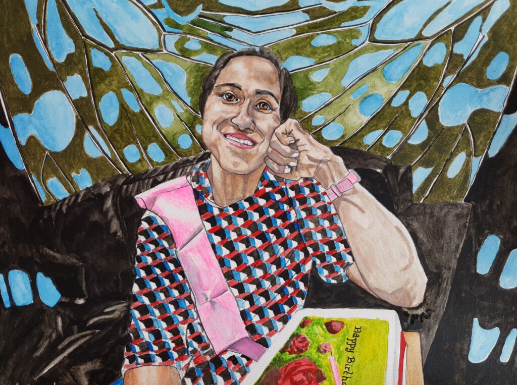 ID Watercolour portrait of beautiful young woman with dark hair tied back. she is resting her face on her fist with elbow resting on the arm of a black, leather couch. In front of her elbow is her Birthday Cake with rose decoration on the top. She is wearing a dress which is based on a geometric pattern of cubes, with the sides being different colours. She is wearing a pink sash and watch. In the background are painted close up of butterfly wings.